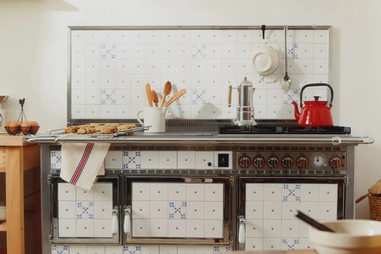 Cuisinière ancienne à motifs bleus, avec bouilloire rouge et ustensiles en bois.