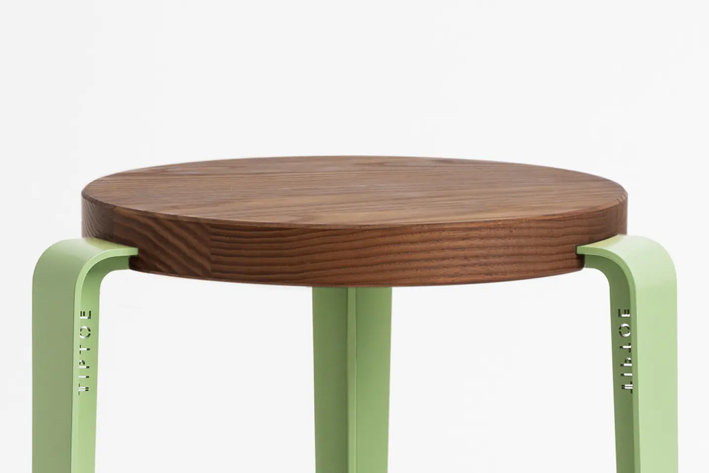 Tabouret rond en bois foncé avec pieds fins vert amande, sur fond clair.