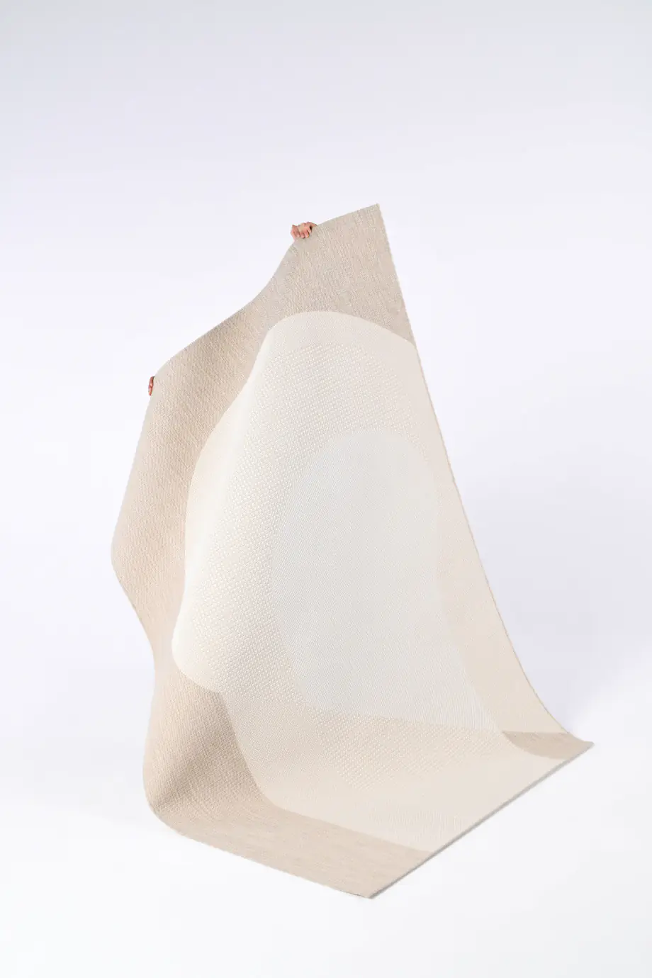 Tissu beige plié en forme géométrique dynamique, sur fond clair.
